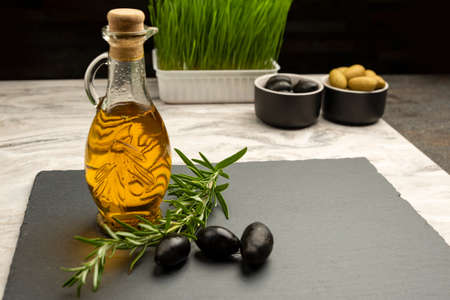 Olive oil. Olives on a background of olive oil. A bottle pours oil into a saucer close-up. Black stone table top with place for text or designの写真素材
