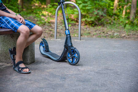 Walk in the park on a scooter. A young guy sits on a bench and rests while walking on a smokat....