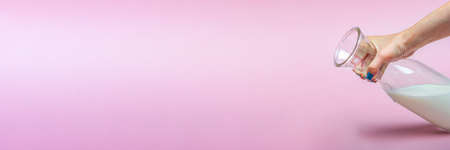 A jug of milk on a pink background in a womans hand. Milk in a glass bottle. Space for text, large banner.の写真素材