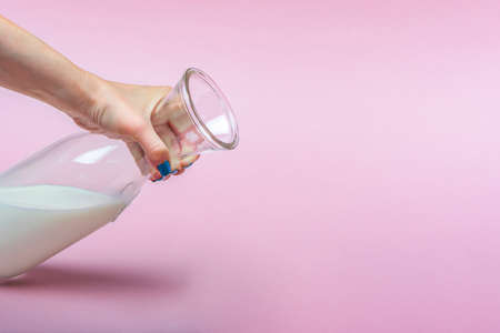A jug of milk on a pink background in a womans hand. Milk in a glass bottle. Space for text, large banner.の写真素材