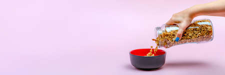 Muesli on a pink background. Pour dry muesli flakes by hand into a bowl. Pouring muesli from a glass...
