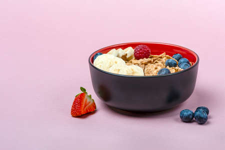 Muesli. Breakfast, healthy food and diet. Muesli with fruits in a plate on a pink background. Blueberries, strawberries and raspberries on a background of muesli flakes. Print banner with copy spaceの写真素材
