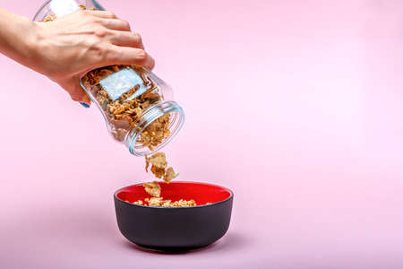 Muesli on a pink background. Pour dry muesli flakes by hand into a bowl. Pouring muesli from a glass...