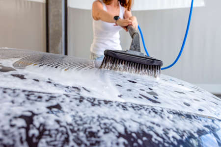 The woman washes the car. A woman at a car wash washes her car with a brush with car shampoo. To advertise a car wash or banner.の写真素材