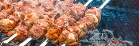 Cooking barbecue, grilled meat barbecue. Cooking pork shashlik on metal skewers. Smoke from embers builds up over the dish. Advertising banner with copy space.の写真素材