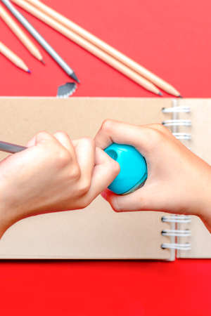 Sharpen pencils. The childs hands sharpen a pencil at school in the lesson. In the background, a...