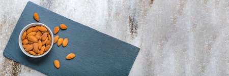 Almonds in a saucer on a black stone table top. Almonds are scattered on the table. Copy space,...