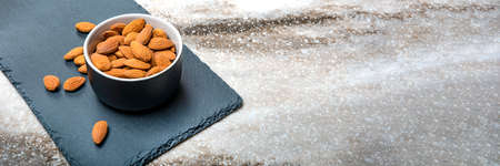 Almonds in a saucer on a black stone table top. Almonds are scattered on the table. Copy space,...