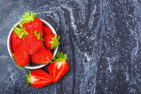 Strawberries on black marble. Ripe strawberries in a saucer on a black background. Place to insert textの写真素材