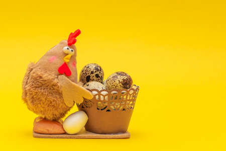Chicken with Easter eggs in a basket. Easter theme on yellow background. The toy chicken is holding a basket of eggs. Place for your text.の写真素材