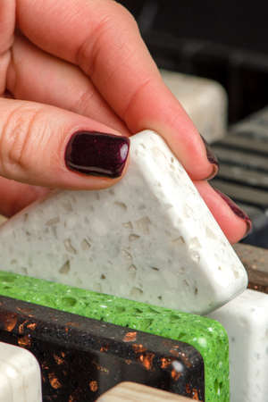 A woman chooses stone samples for a kitchen countertop. A set of multi-colored samples of artificial...