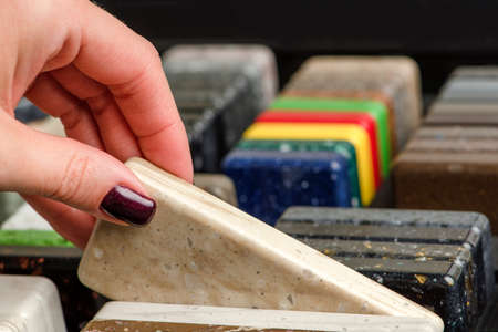 A woman chooses stone samples for a kitchen countertop. A set of multi-colored samples of artificial...