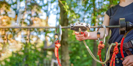 Woman hangs a carabiner on a rope in a forest adventure park. Using climbing equipment: carabiner, belt, rope. Banner for advertising, design or website headerの写真素材