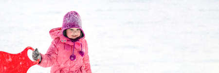 A girl in pink clothes rides on a snowy slide in winter. White girl 5 years old sledding in winter...