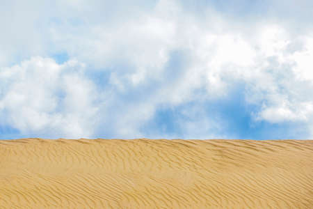 Desert landscape with blue sky and yellow sand. Background of dunes and blue sky with clouds. There...