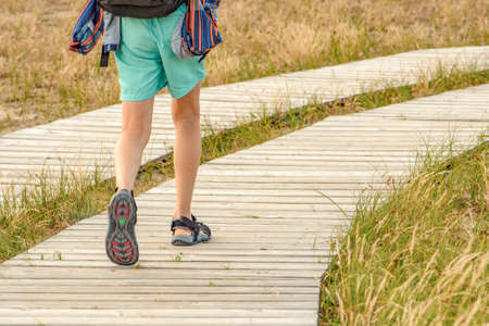 Wooden path in the mountains. Winding tourist path made of boards in the mountains. Legs of a young guy 10 years old close-up go to the mountains along a tourist route with a backpackの写真素材