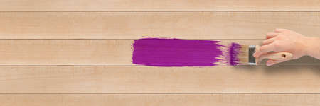 Close-up of a brush in the hand of a person painting a wooden board, hobby and renovation concept. A...