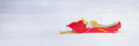 Red sled with snow on a white snowy background. Entertainment in winter for children. Red-yellow plastic sledの写真素材