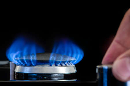Gas stove on a black background. Fragment of a gas kitchen stove with a blue flame, close-up. Energy...
