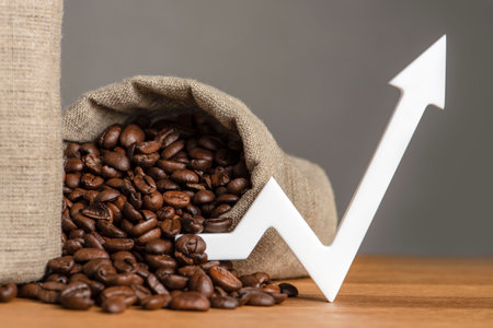 A bag of coffee beans and a chart arrow pointing up. The cost of coffee in the markets of the world. The concept of the growth of the cost of coffee beansの写真素材