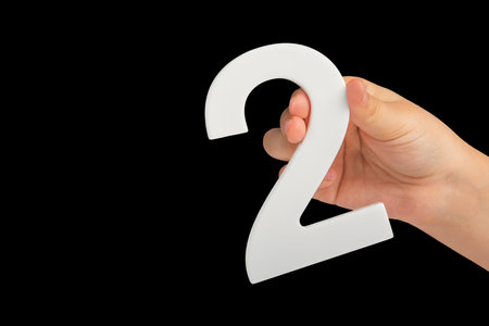 number two in hand isolated on black background. Number two white in a childs hand on a black background. For inserting into a project or design.の写真素材