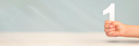 Number one in hand. A hand holds a white number one on a blurred background with copy space. Concept with number one. 1 percent rate, birthday, first or winner.の写真素材