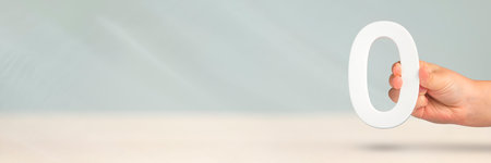 Numeral zero in hand. A hand holds a white number zero on a blurred background with copy space. Zero concept, 0 percent interest rate, minimum air emissions, cost or credit no increase.の写真素材