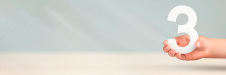 Number three in hand. Hand holding white number 3 on blurred background with copy space. Concept...