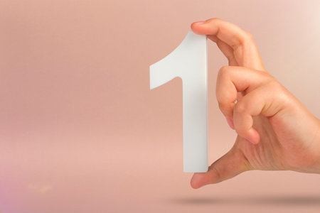 Number one in hand. A hand holds a white number one on a red background with copy space. Concept with number one. 1 percent rate, birthday, first or winner.の写真素材