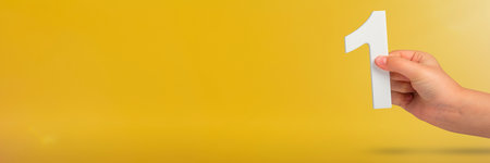 Number one in hand. A hand holds a white number one on a yellow background with copy space. Concept with number one. 1 percent rate, birthday, first or winner.の写真素材