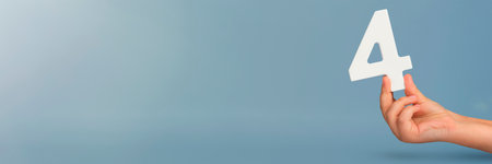 number four in hand. Hand holding white number 4 on blue background with copy space. Concept with number four. Birthday 4 years, fourth grade, four day work weekの写真素材