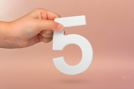 Number five in hand. Hand holding white number 5 on red background with copy space. Concept with number five. Birthday 5 years, fifth grade, five day work weekの写真素材