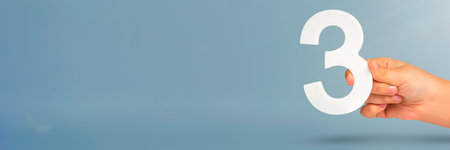 Number three in hand. Hand holding white number 3 on blue background with copy space. Concept with number three. 3 percent, birthday 3 years, third grade, tripleの写真素材