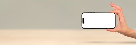 Phone in hand on a white background. A womans hand holds a new modern phone in her hand on a white background with a blank white screen.の写真素材