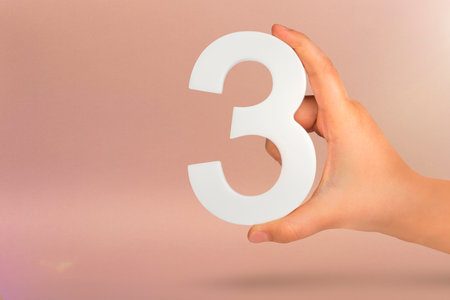 Number three in hand. Hand holding white number 3 on red background with copy space. Concept with number three. 3 percent, birthday 3 years, third grade, tripleの写真素材