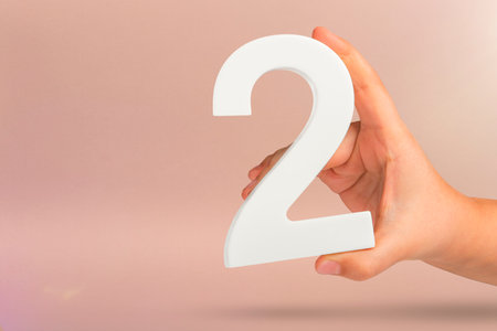 Number two in hand. Hand holding white number 2 on red background with copy space. Concept with number two. 2 percent, birthday 2 years old, couple, two, doubleの写真素材