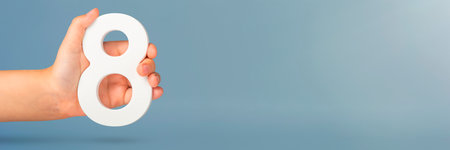 Eight in hand. A hand holds a white number 8 on a blue background. Concept with number eight. Birthday 8 years, percentage, eighth grade or day, international womens day.の写真素材