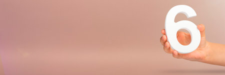 Number six in hand. A hand holds a white number 6 on a red background with copy space. Concept with number six. 6 percent, birthday 6, sixth grade, in sixth gradeの写真素材