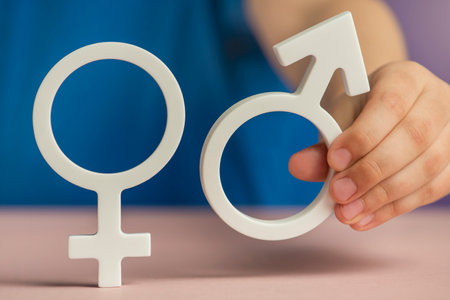 The concept of gender equality. Symbol of female and male gender in hand as a symbol of equality of rights. On a purple background in a blue t-shirt with copy spaceの写真素材
