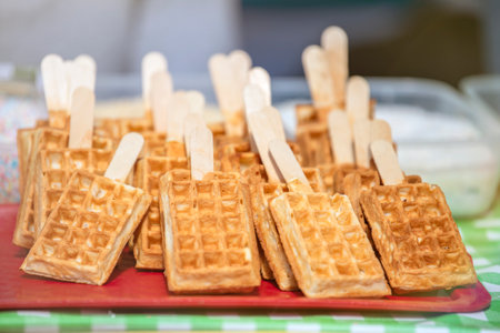 Belgian waffles on a wooden stick covered with chocolate icing. Production and sale of fresh Belgian waffles in a pastry shop.の写真素材