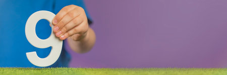 Number 9 in hand. A hand holds a white number nine on a purple background, nine percent per annum. Advertising banner or greeting card. Concept for Europe Day, May 9th.の写真素材