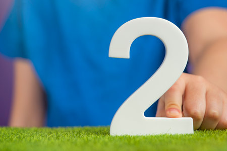 White number 2 in hand. The hand holding the number 2 symbolizes choice, partnership and duality, the choice between two alternatives, to combine the efforts of two people to achieve a common goal.の写真素材
