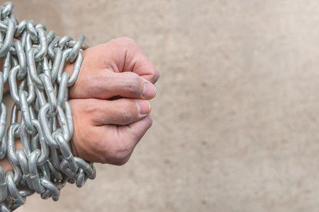 The rough hands of a worker, a white male are wrapped in a chain as a concept of slavery or...