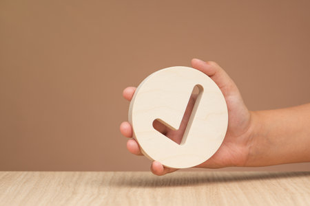 Hand holding check mark icon, banner with wooden check mark icon in hand, right sign. On a brown background. Copy space. Place for textの写真素材