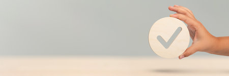 Hand holding check mark icon, banner with wooden check mark icon in hand, right sign. On a blue background. Copy space. Place for textの写真素材