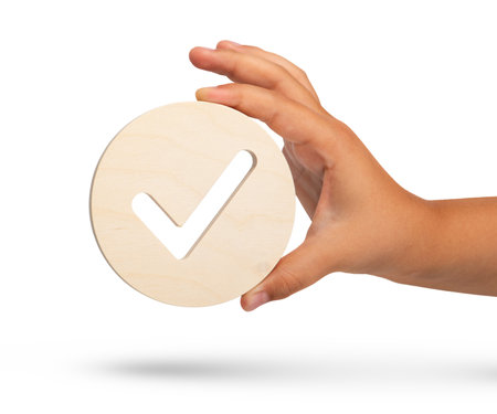 Check mark symbol on white isolated background. Big wooden round badge check stamp in hand close up.の写真素材