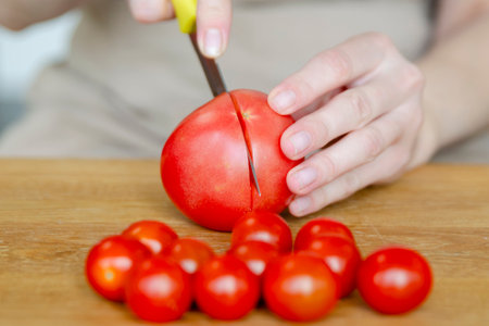 Preparing summer salad with tomatoes close-up. A womans hands cut a tomato in half for a salad or side dish.の写真素材