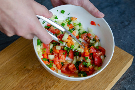 The process of mixing salad. Close-up of a mans hands stirring a salad mixture. Hands stir the salad so that the ingredients are distributed throughout the plate.の写真素材