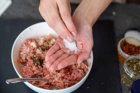 A womans hand sprinkles salt on a raw meat close-up. Salt is used as a raw meat dressing.の写真素材