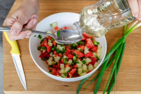 A womans hands pour a couple of large spoons of oil, close-up, to make the salad juicier and tastier. High quality photo.の写真素材